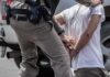 Police officer handcuffing person against vehicle wheel