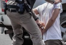 Police officer handcuffing person against vehicle wheel