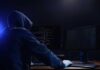 Hooded figure using dual monitors in dark room