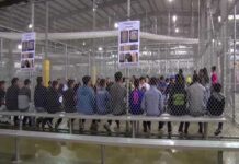illegal immigrants are sitting on benches inside a fenced facility