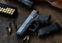 Handgun with ammunition magazine and rifle on wooden table