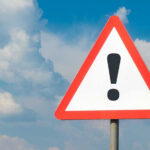 Warning sign with exclamation mark against cloudy sky