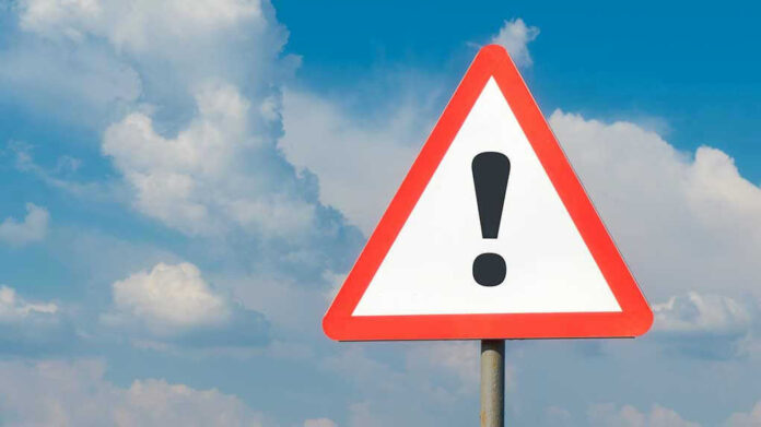 Warning sign with exclamation mark against cloudy sky