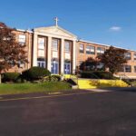 Exterior view of a brick school building with yellow steps and a cross on top