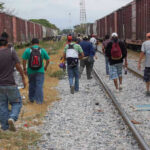 People walking along train tracks carrying backpacks