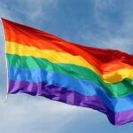 A rainbow flag waving against a blue sky