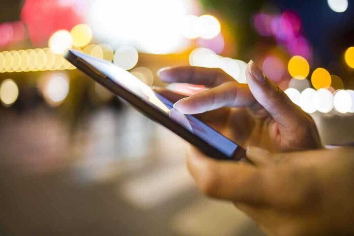 A person's hand using a smartphone in a city at night with blurred lights in the background