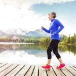 Senior woman jogging along a lakeside with mountains in the background