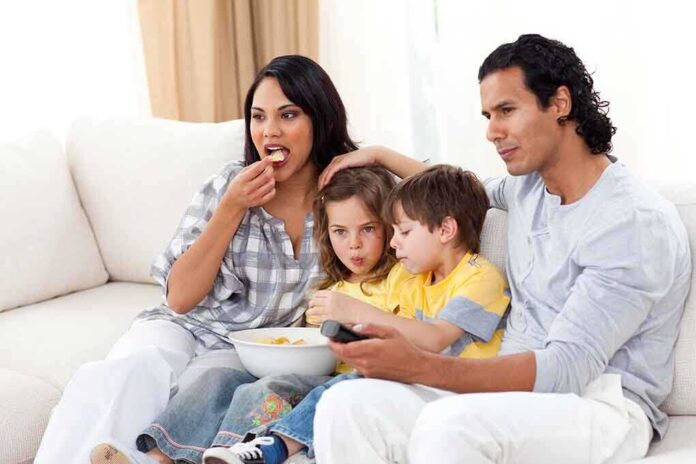 A family of four enjoying a movie night on the couch with snacks