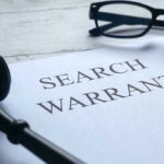 Search warrant document with gavel and glasses.
