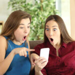 Two women look surprised at a phone.