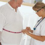 A healthcare professional measuring a patients waist with a tape measure