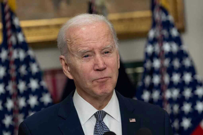 Man in suit speaking, flanked by American flags.