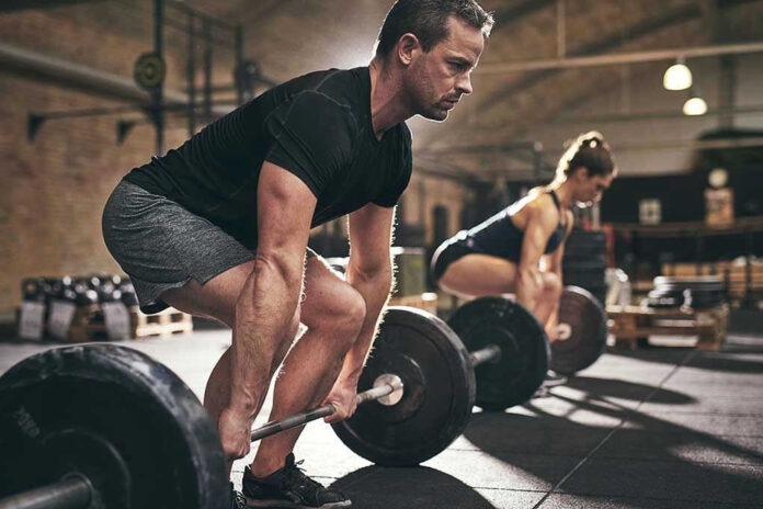 Man and woman lifting barbells in gym.