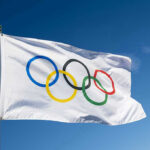 American Olympians TRASH Country As Dems and Media Gush Olympic flag waving against clear blue sky.