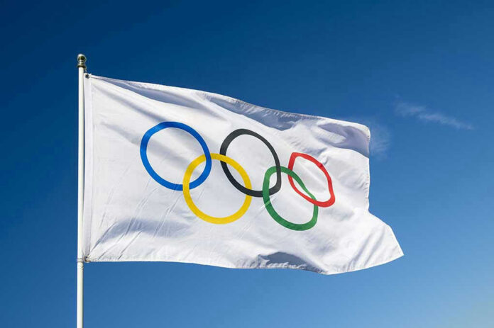 Olympic flag waving against clear blue sky.