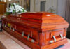 Congressman DIES Aged 86, Cause Of Death Revealed Wooden casket with white flowers in a funeral home.