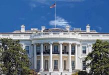 The White House with the American flag flying against a blue sky