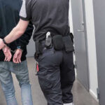 Plane Hijacker Awaiting Deportation Released by Activist Judge Officer escorting handcuffed person down hallway.
