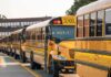 Row of yellow school buses parked outside a brick school