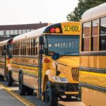 Row of yellow school buses parked outside a brick school