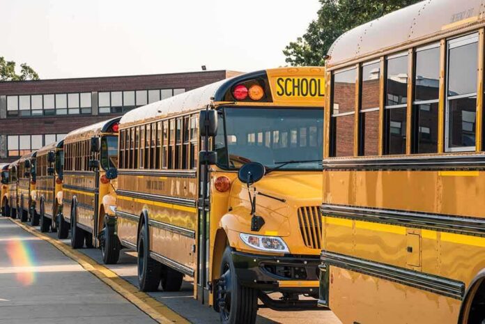 Row of yellow school buses parked outside a brick school