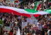 Crowd of protesters holding signs and a large tricolor flag