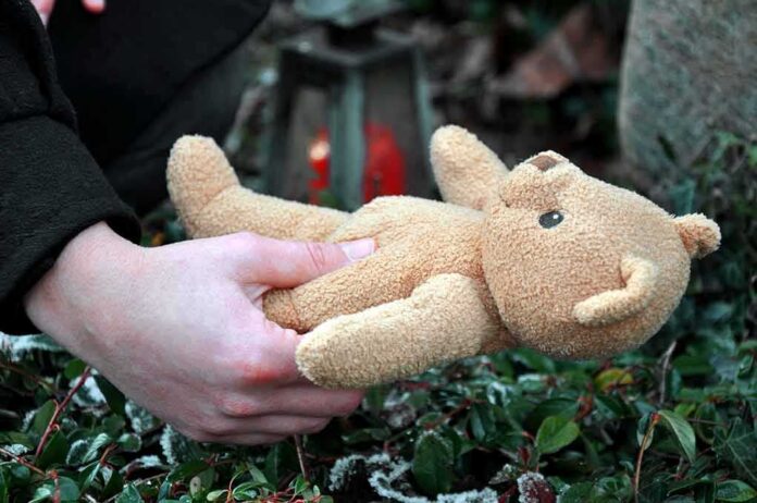 Hands holding a teddy bear near a grave
