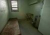 Empty jail cell with bed, barred window, and stainless steel toilet
