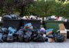 Overflowing dumpsters with piles of trash bags and cardboard