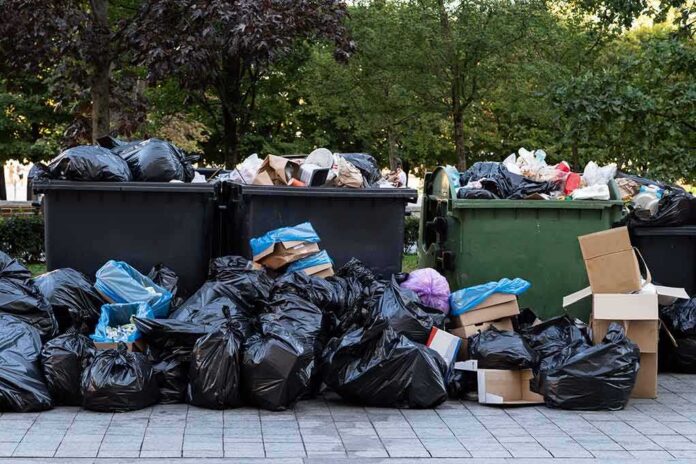 Overflowing dumpsters with piles of trash bags and cardboard