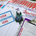 Trump Conducts MASS LAYOFFS Weeks Before Midterms Voter registration table with forms, pens, and informational materials