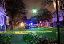 Police car blocks residential street at night behind caution tape