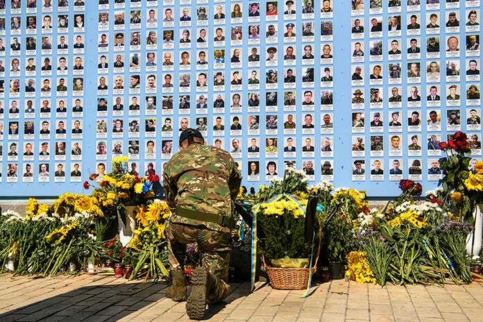 Soldier kneels at memorial wall with photos and flowers
