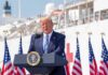 Trump Slashes Biden Rule – Says He Can Do It Better Donald Trump speaking at a podium with American flags and a ship in the background
