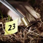 Forensic gloved hand collecting a bullet casing near evidence marker