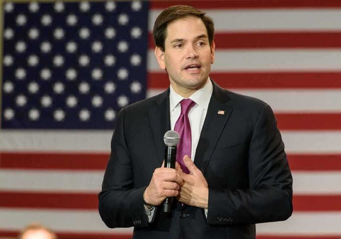 man in suit speaking with microphone before American flag