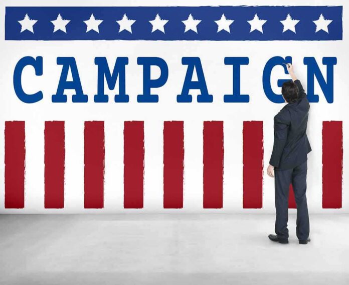 shutterstock_486646441-2 Man in suit writing on large campaign banner with stars and stripes
