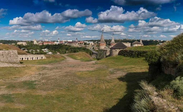shutterstock_770540464 Medieval stone castle with towers on a grassy hill under a cloudy sky