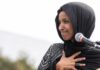 Ilhan Omar speaking at a microphone with hand on chest