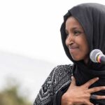 FBI Raid Hits Ilhan Omar’s Home Ilhan Omar speaking at a microphone with hand on chest