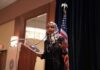 Ilhan Omar Breaks Silence After Feds Raid Ilhan Omar speaking at a podium with a microphone