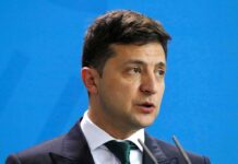 Volodymyr Zelensky speaking at a podium against a blue backdrop