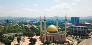 Golden-domed mosque with four minarets in a modern cityscape