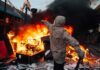 Hooded person throws object near street fire