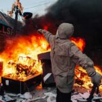 France Descends into CHOAS – Riots Erupt into War Hooded person throws object near street fire