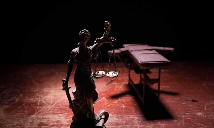 Lady Justice statue with scales in dramatic light beside an empty gurney