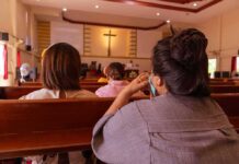 Woke Senate Candidate Calls for Repentance Over White Privilege people seated in church pews facing a cross