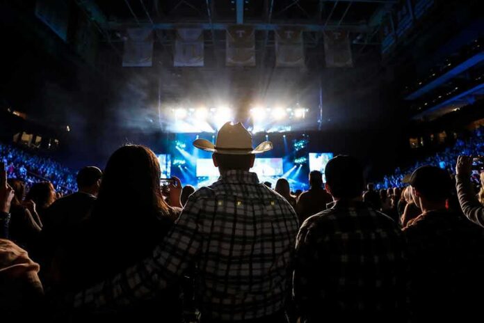 shutterstock_2150018925 Cowboy-hatted man watches a concert in a packed arena