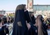 Women in black veils standing in a crowded outdoor gathering